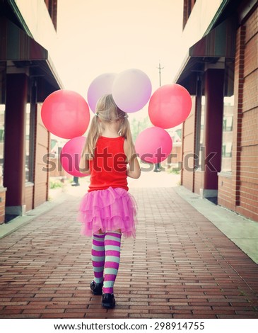 A little girl is holding colorful balloons walking down a brick road outside for a happiness or freedom concept.