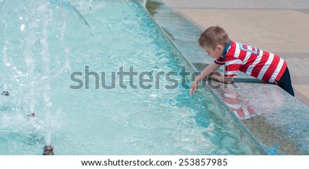 Happy little boy playing with water of fountain