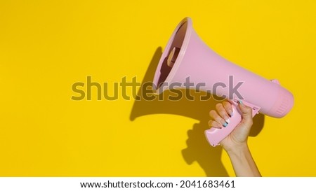 A woman's hand holding a pink megaphone isolated on a yellow background. Creative announcement concept. Loud voice of women. Women's rights and voice. Advertisement mock up with copy space for text.