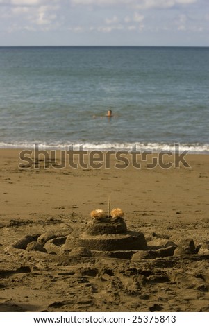 A sand castle in the foreground and a soft focus person floating in the ocean in the background
