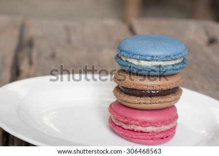 Three colorful macaron - Blue macaron vanilla flavor, pink macaron strawberry flavor and brown macaron chocolate flavor stacked on the plate