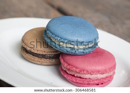 Three colorful macaron - Blue macaron vanilla flavor, pink macaron strawberry flavor and brown macaron chocolate flavor on the plate, blue macaron on top.