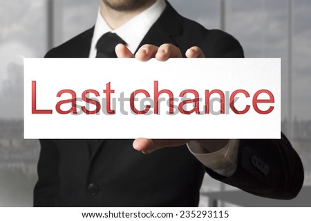 businessman in black suit holding sign last chance