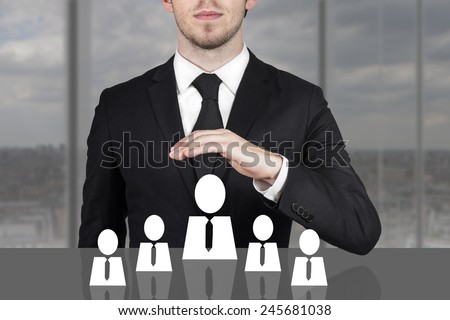 businessman in black suit holding protective hand above employee staff