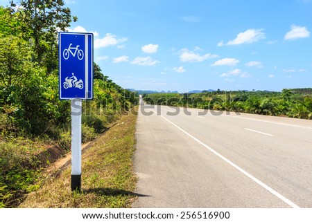 bike and motorcycle traffic sign side asphalt road through the green field and clouds on blue sky in summer day