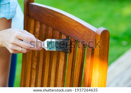 female hand holding a brush applying varnish paint on a wooden garden chair - painting and caring for wood with oil Foto stock © 