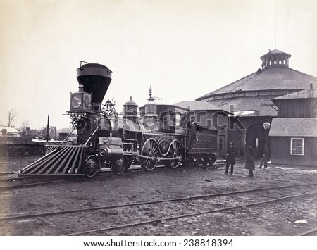 Engine, J.H. Devereux, of the United States Military Railroad with two crew members on board outside the roundhouse at the Alexandria station. Albumen print, photo by Andrew J. Russell, ca. 1860s