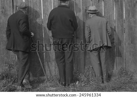 The backs of three men watching a football game through cracks in a fence. Star City, West Virginia. Oct. 1935 photo by Ben Shahn.