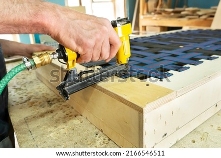 Stapling elastic band with a yellow pneumatic stapler. Furniture manufacture shot. Selective focus Foto stock © 