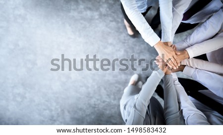 Photo of Close up top view of young business people putting their hands together. Stack of hands. Unity and teamwork concept.