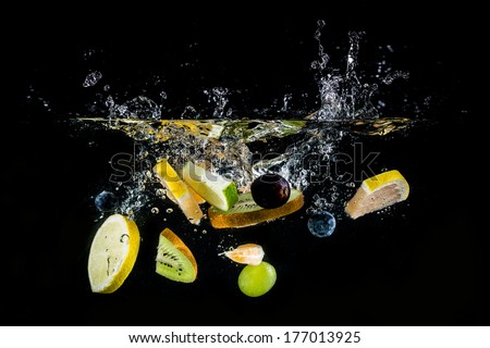 Splashing fresh fruit on water on black background