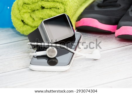 Fitness equipment, smart watch and phone on wood background.