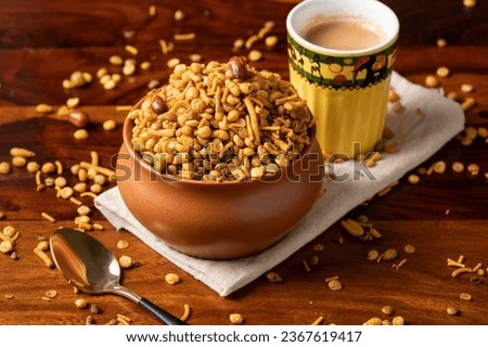 Traditional Indian deep fried salty and spicy dish- Chivda or mixture or farsan or namkeen made of gram flour and mixed with nuts. Served with hot cup of tea, brass spoon to eat on wooden surface Сток-фото © 