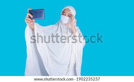 Ied Fitr , Ied Mubarak , Asian muslim woman with face mask having a video call with her family, smiling and waving.  Imagine de stoc © 
