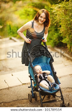 Happy young mother with baby in buggy walking in park