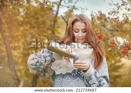 beautiful woman drinking tea from thermos in the forest