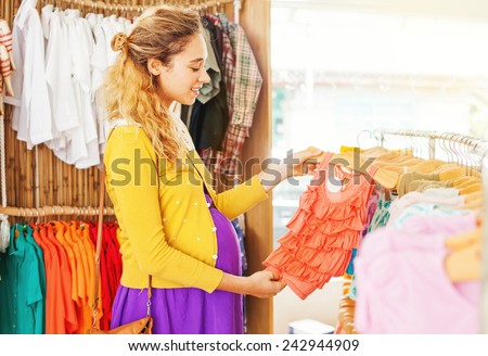 Pretty stylish pregnant woman choosing clothes in the shop for her future newborn daughter