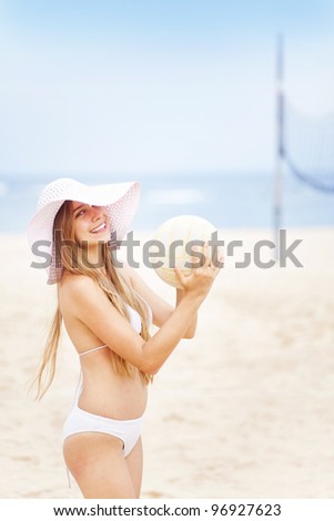 Cute cheerful girl with ball near volleyball net on the beach