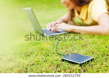 woman using hard drive disk to backup her data while lying down relaxed on a grass