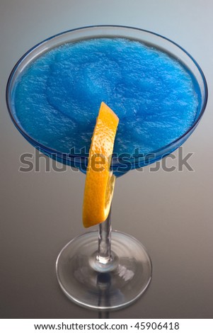 Frozen Blue Hawaiian mixed drink with orange slice garnish on grey background with reflection