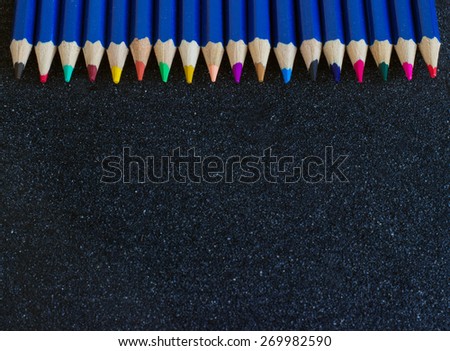 A rainbow of colored pencils, on a dark black background.