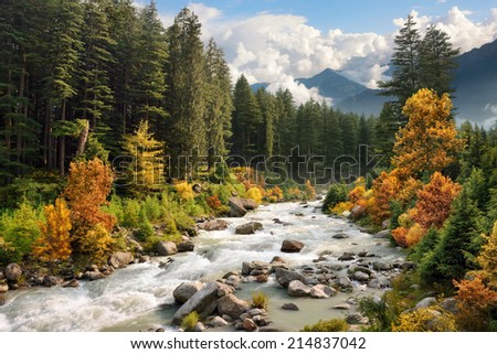 Beautiful colorful landscape with a stream and forest in autumn colors, mountains in the background and blue sky with white clouds