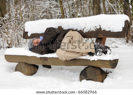 Exhausted young man sleeping on a snow-covered bench, ignoring the chill