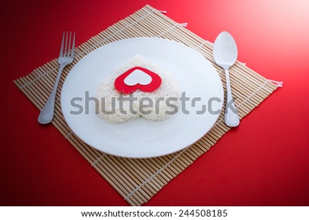 cooked rice heart shapes with a spoon and fork on white dish  in Platemat and on red background