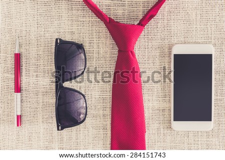 red pen, smartphone, sunglasses on clean sackcloth with red necktie. Young business concept. Photo retro style