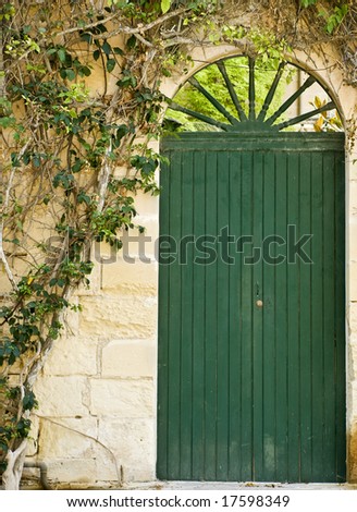 A medieval garden door painted in deep green next to climbing plant