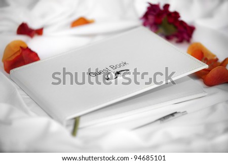 Wedding guest book laid on white silk and surrounded by flower petals