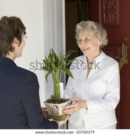 Attractive senior woman receiving gift of bamboo plant at front door