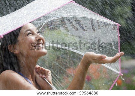 Beautiful young woman grins as she holds out her palm to catch falling water. She is holding an umbrella over her head. Horizontal shot.