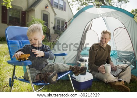 Father with laptop and son playing while camping in the front yard