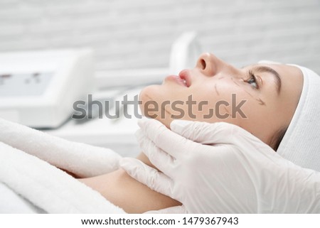 Closeup of beautiful female client with markup on face lying on coach while visiting surgeon in clinic. Young woman doing lifting and cosmetic procedures n beauty salon. Concept of facials. Foto stock © 