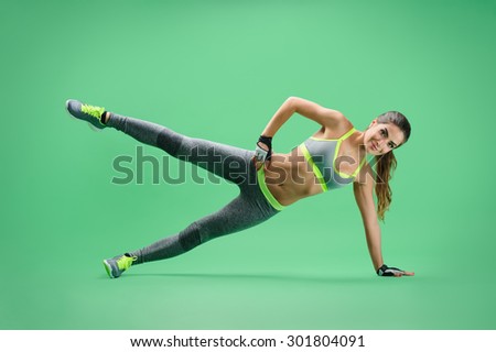 sportswoman performs the side rack with an emphasis on her left arm and leg, right hand on the waist, the right leg is raised to shoulder level; sportswoman on a green background in a gray sports suit