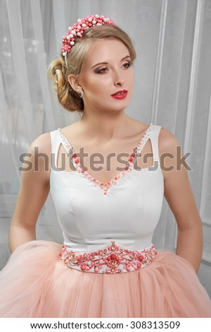 Young beautiful, pretty woman in light pink short dress with red embroidery, hands on hips; on hills,  portrait; makeup, hairstyle, in the room .