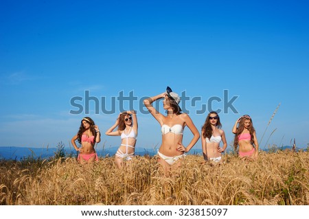 Group photo of charming young girls in bikinis, beautiful sexy models, they smile, posing in wheat field on a background of blue sky.