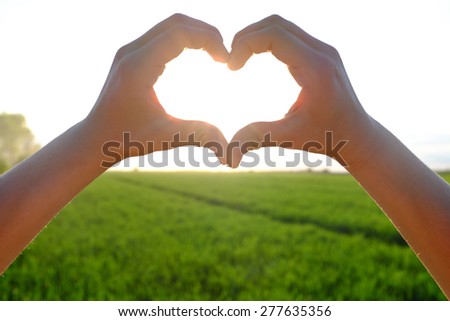 Hands forming a heart shape with sun in the background and field