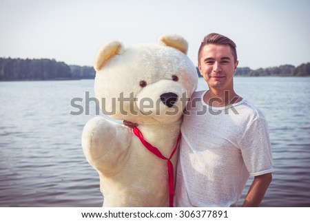 Handsome young man is fooling around with his massive teddy bear.