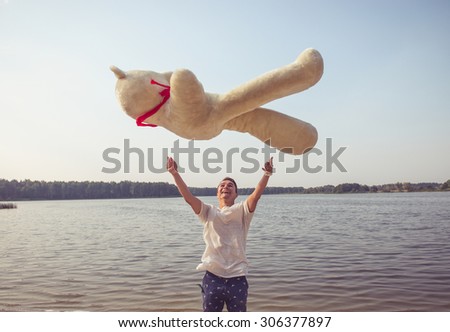 Handsome young man is fooling around with his massive teddy bear.