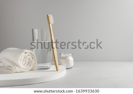 Bamboo toothbrush, glass of water, white a cotton towel and powder for brushing your teeth in jar. light gray concrete surface, gray backdrop. Biodegradable personal care products. No plastic concept.