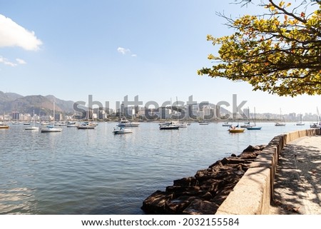 Beautiful view of a sunny morning in Urca, Rio de Janeiro, from where you can see a blue sky, the bay, colorful boats, reflections, hills, city buildings, trees, and the sidewalk. Imagine de stoc © 