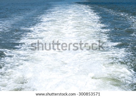 WAKE - WHITE FOAM WATER FROM A BOAT IN BLUE SEA