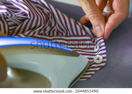 Ironing the sleeve of a shirt with a steam iron. Woman ironing shirt on ironing board with steaming iron