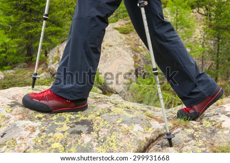 Poles and hiking boot closeup on mountain rocks, nordic walking, hiking.