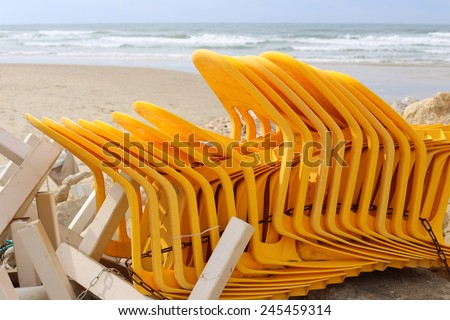 Yellow plastic chairs stacked, tied with a chain on the beach out of bathing season, along with other Kiosk Furniture in \'Herzliya beach\', Israel.