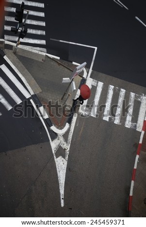 Top view of black & White cross road: Traffic island, pedestrian crossings and traffic lights on a rainy day. A Pedestrian with a red umbrella cross the street.
