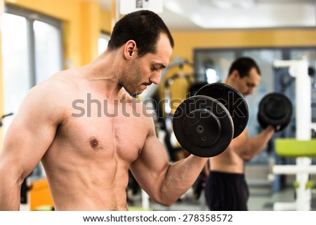 Muscular power athletic male bodybuilder training his biceps with dumbbells in fitness center
