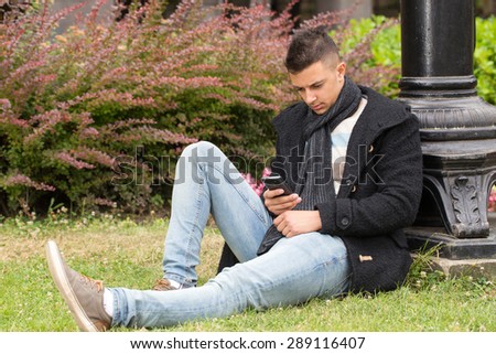 young handsome man writing sms in park, sitting beside a street lamp